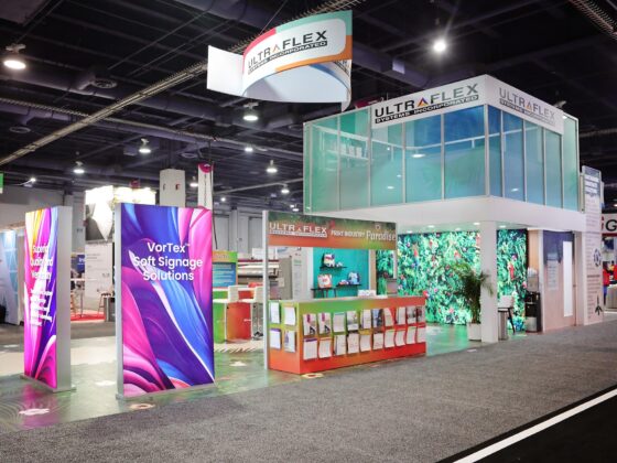 UltraFlex Systems trade show booth at PRINTING United, with backlit and front-lit VorTex soft signage SEG panels in aluminum frames